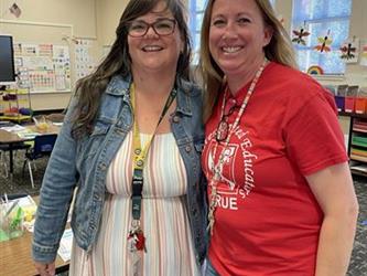 two elementary teachers standing and smiling in school library