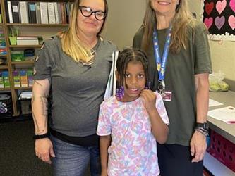 elementary student with parent and teacher standing in school libary smiling